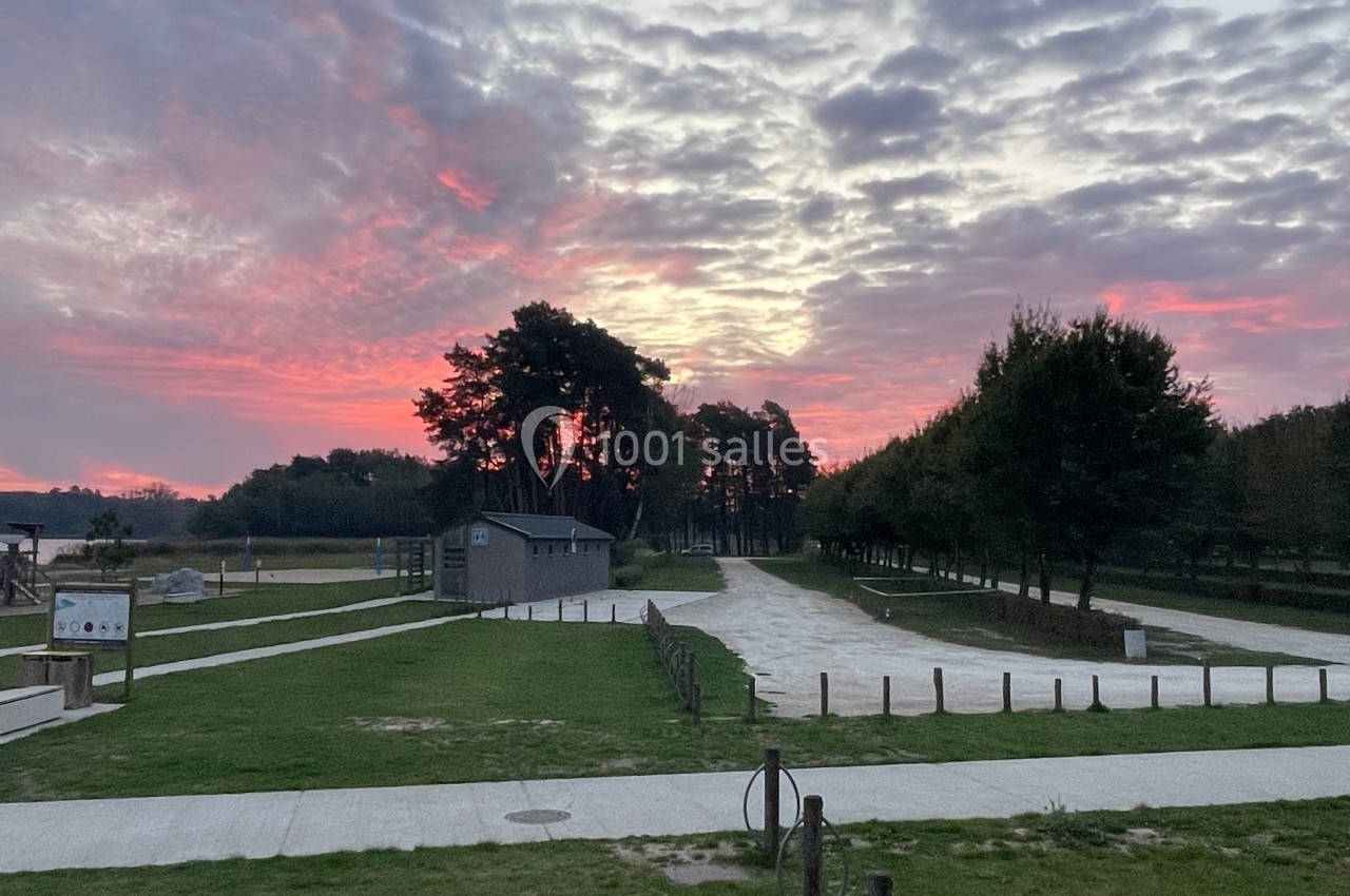 Coucher de soleil coloré sur un parc avec chemins, arbres, bâtiment en bois et aire de jeux en arrière-plan.