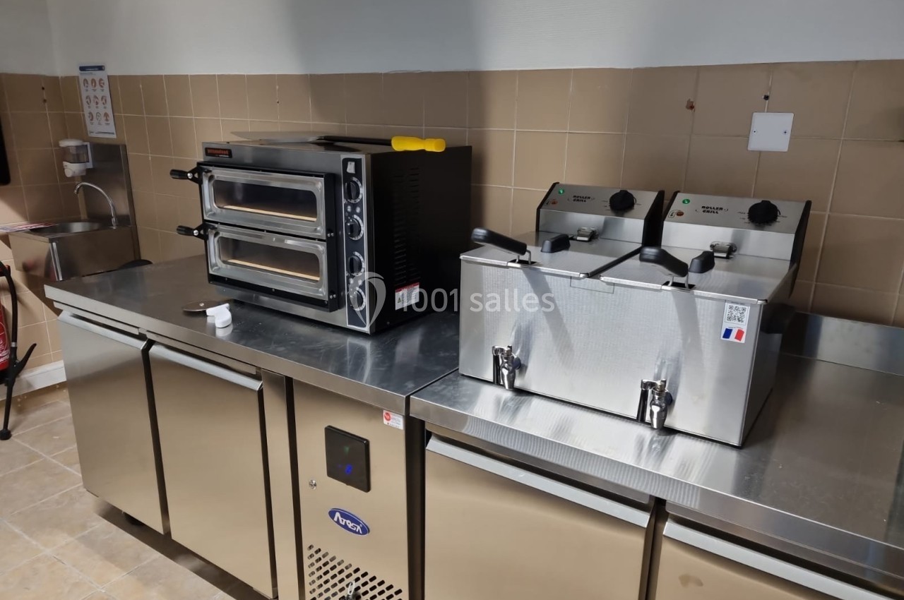 Cuisine professionnelle équipée d'un four à double étage, de deux friteuses et de plans de travail en inox.