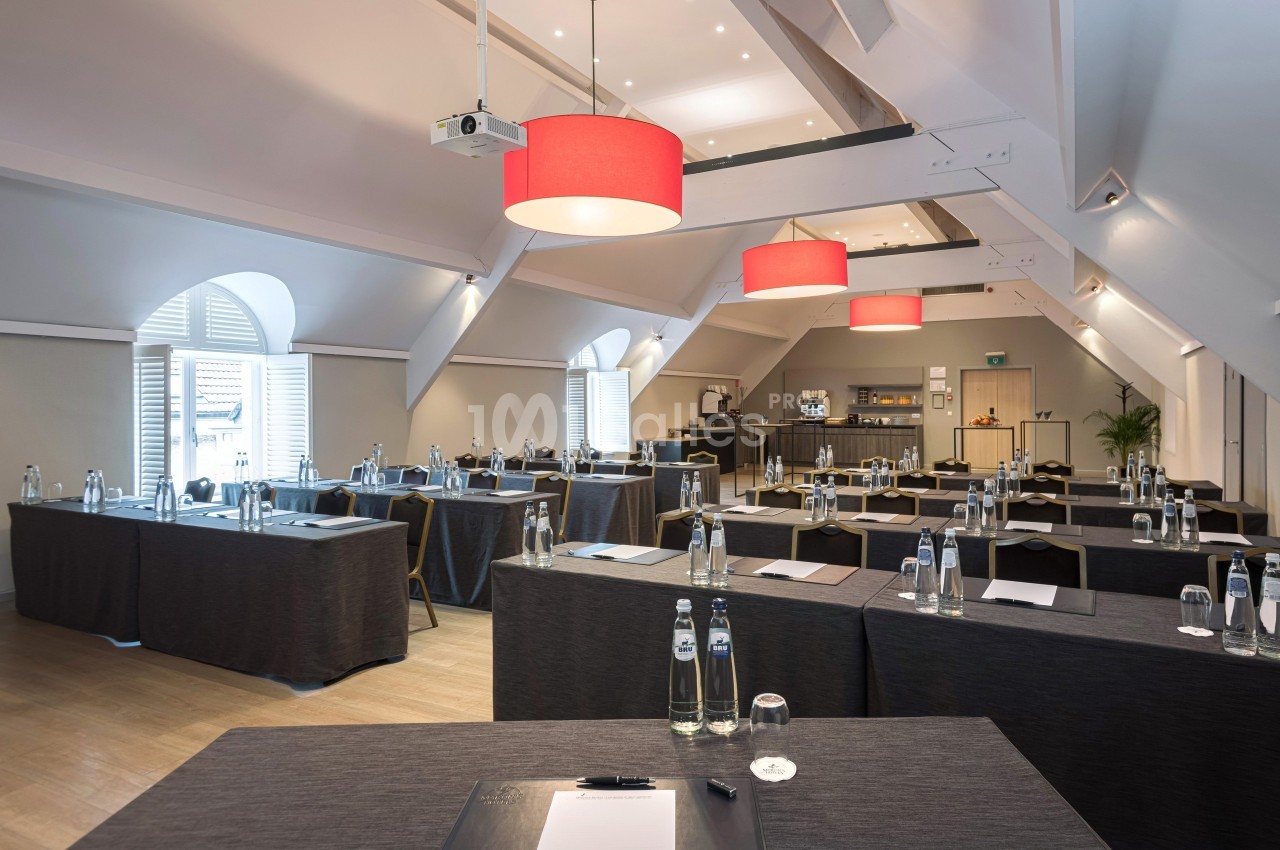 Salle de réunion lumineuse avec tables disposées en rangées, bouteilles d'eau et matériel de prise de notes.