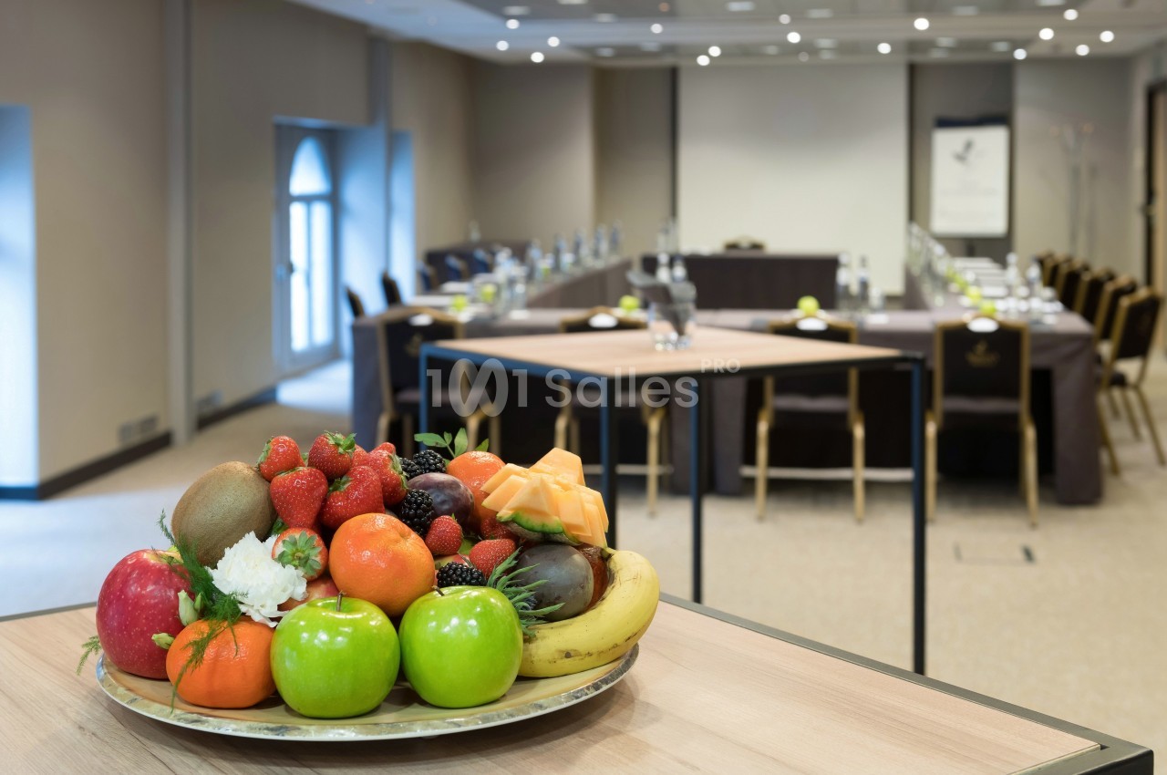 Plateau de fruits variés sur une table en premier plan, avec une salle de réunion aménagée en arrière-plan flou.