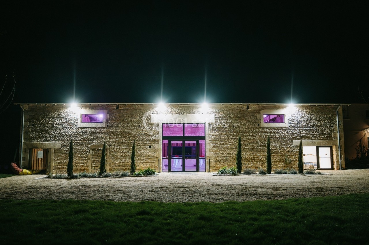 Façade d'un bâtiment en pierre éclairé la nuit, avec des lumières violettes visibles à l'intérieur.