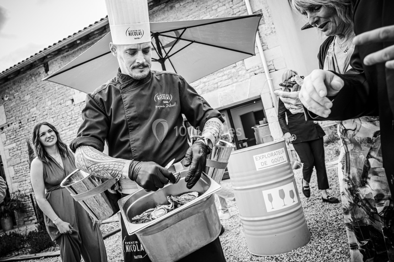 Un chef en tenue professionnelle prépare des huîtres en extérieur lors d'un événement convivial.