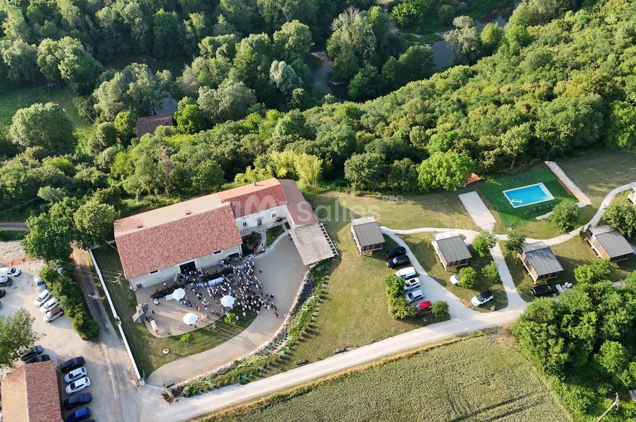 Vue aérienne d'un domaine rural avec bâtiments, piscine, parking et espaces verts entourés de forêt.