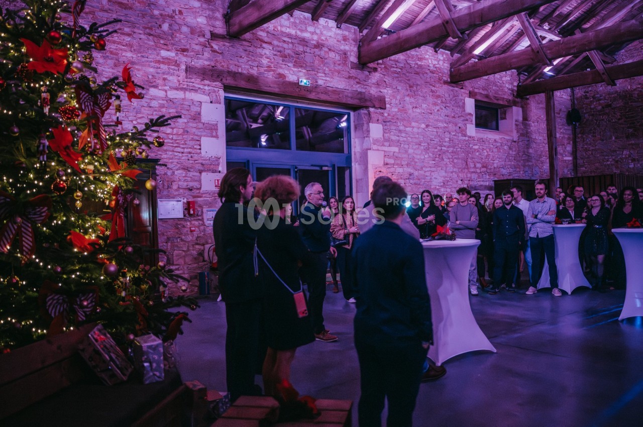 Groupe de personnes réunies dans une salle en pierre, décorée avec un sapin de Noël illuminé.