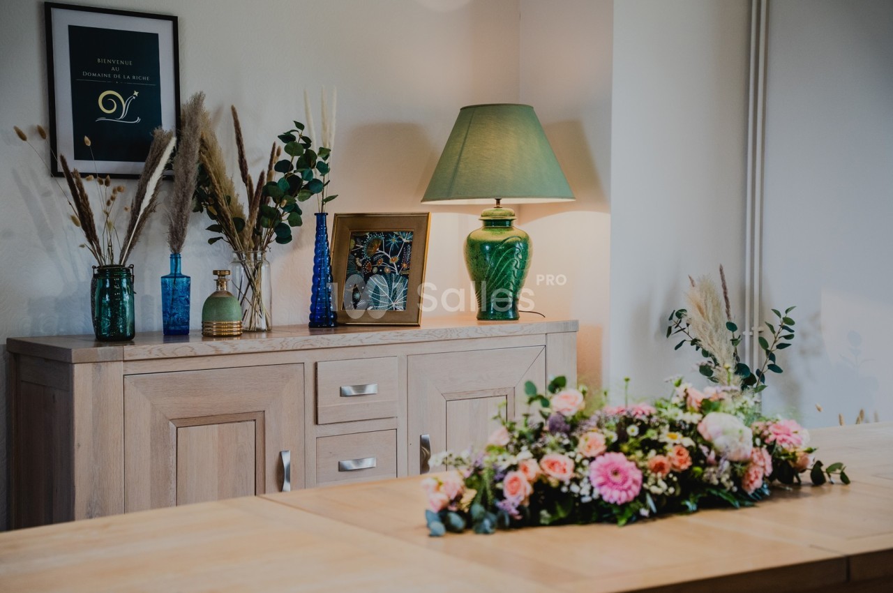 Buffet en bois décoré de vases, lampe verte et cadre, avec un bouquet de fleurs sur une table au premier plan.