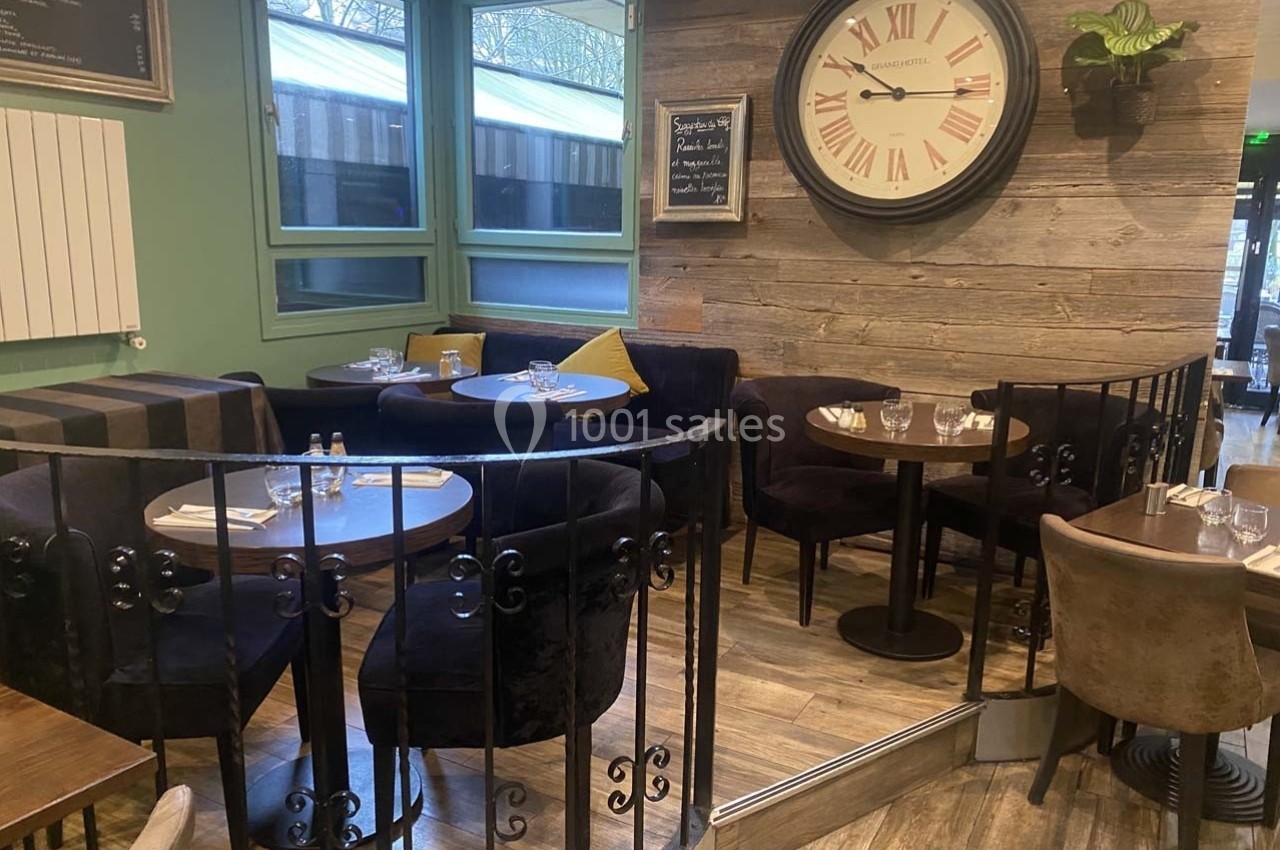 Salle de restaurant avec tables rondes, chaises rembourrées, horloge murale et décoration boisée.