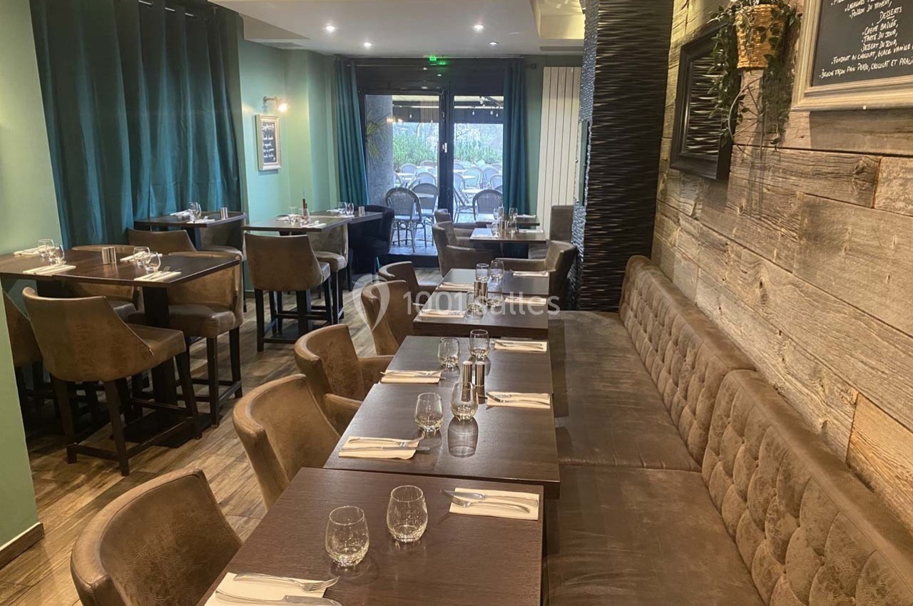Salle de restaurant avec tables dressées, chaises en cuir, banquette et décoration murale en bois.
