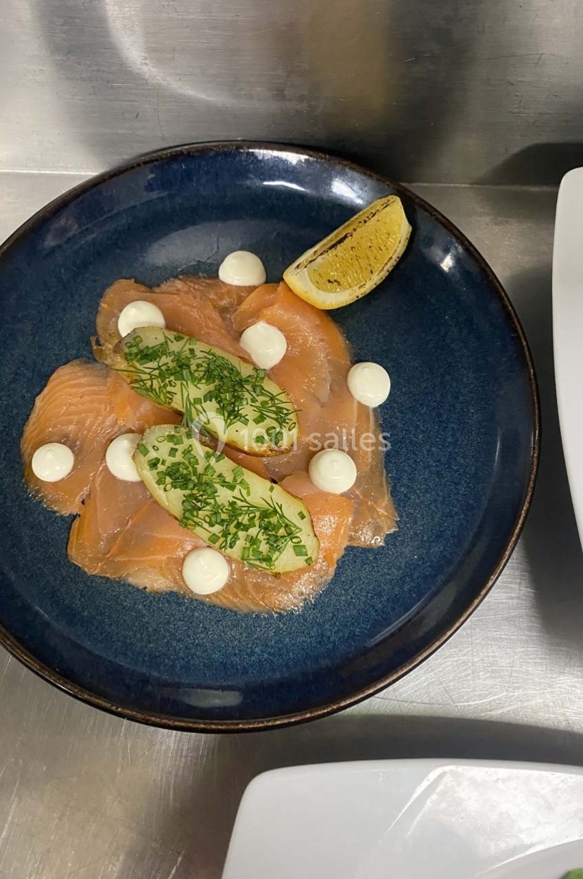 Tranches de saumon fumé garnies d'avocat, herbes fraîches, sauce blanche et un quartier de citron sur une assiette bleue.