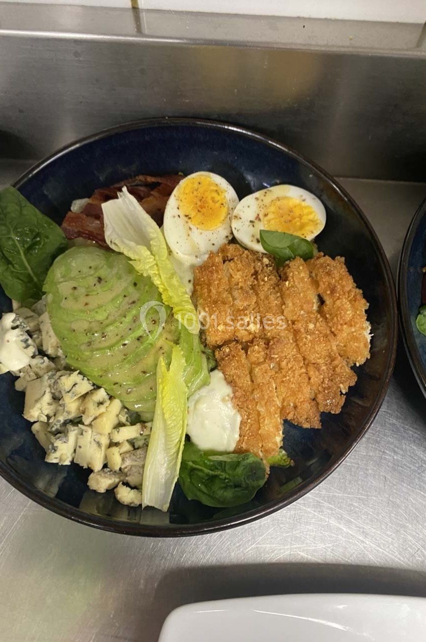 Bol contenant des morceaux de poulet pané, avocat tranché, œuf dur, fromage bleu, salade et sauce.