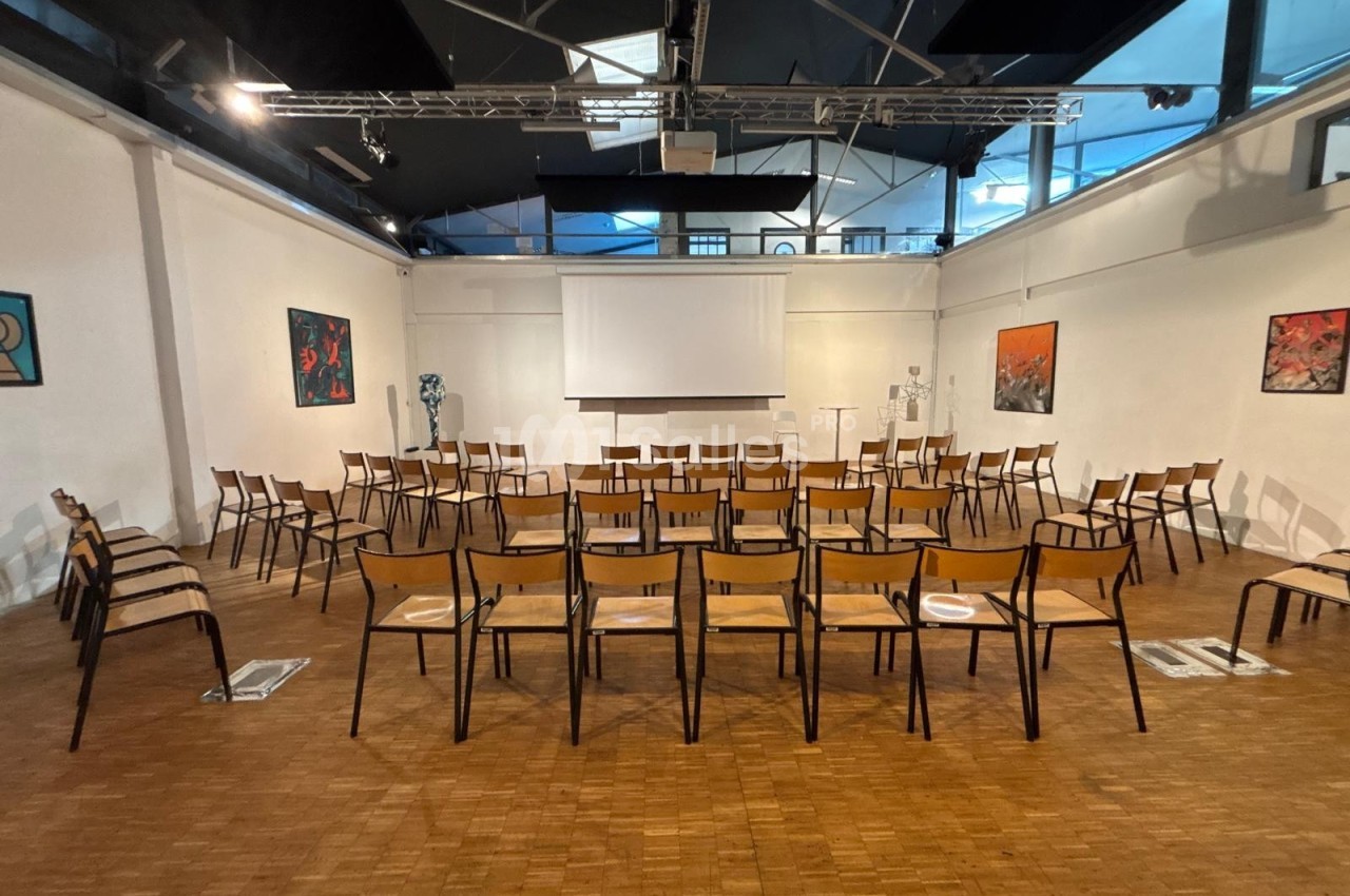 Salle de conférence avec des rangées de chaises en bois, un écran de projection et des œuvres d'art accrochées aux murs.