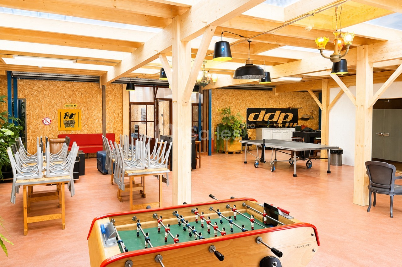Salle lumineuse avec baby-foot, tables empilées, baby-foot et décoration en bois et métal.