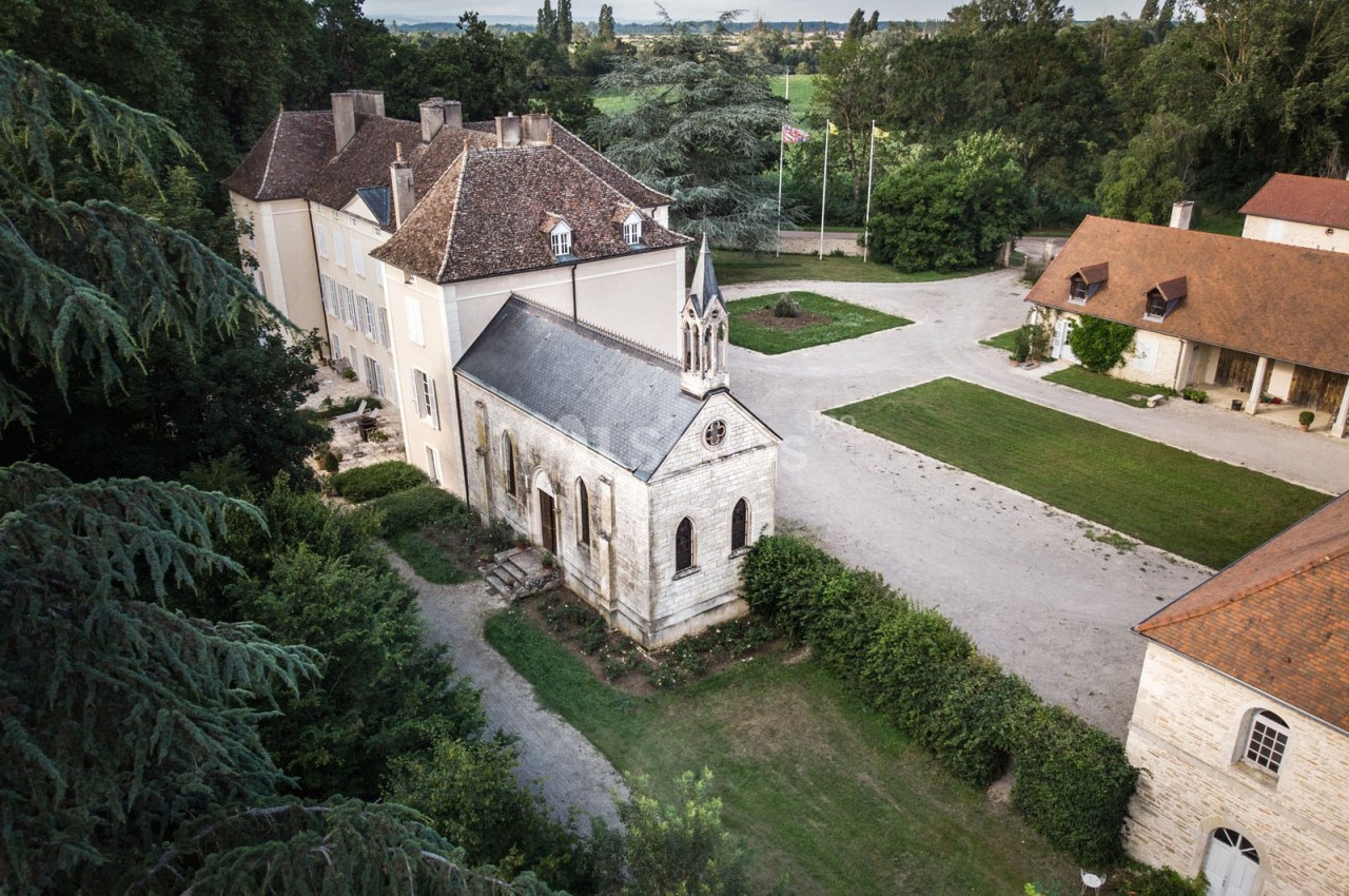 Vue aérienne d'un domaine avec une petite chapelle en pierre, des bâtiments annexes et des espaces verts environnants.