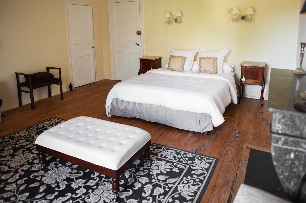 Chambre lumineuse avec lit double, banc capitonné, tapis à motifs et meubles en bois sur un parquet.