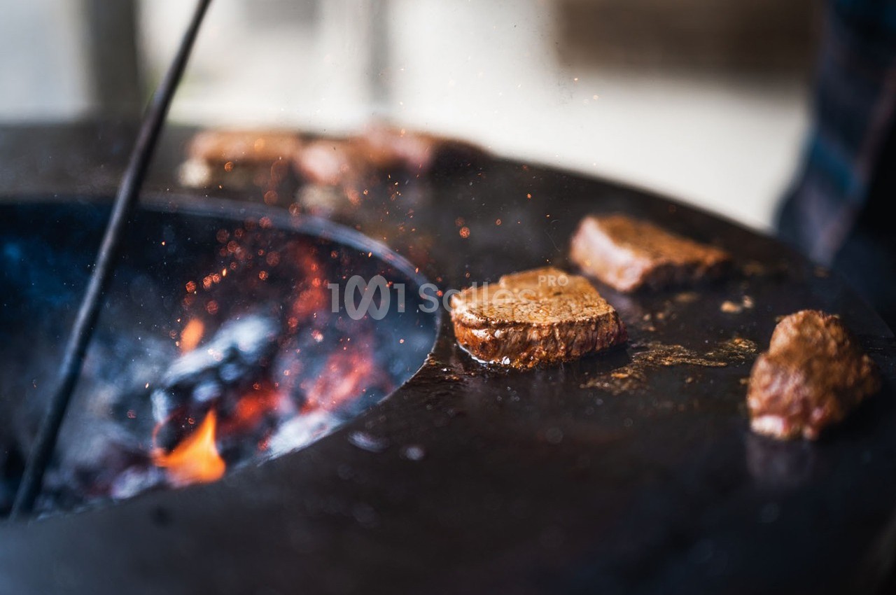 Morceaux de viande grillant sur une plaque chauffante ronde au-dessus d'un feu ouvert.