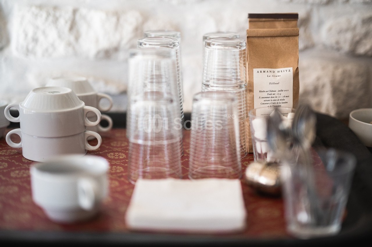 Verres empilés, tasses blanches et sachet de café disposés sur un plateau avec une nappe rouge.