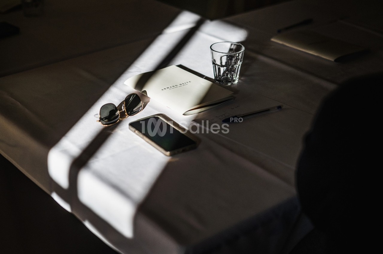 Objets sur une table éclairée par une lumière naturelle : lunettes de soleil, carnet, stylo, verre et smartphone.