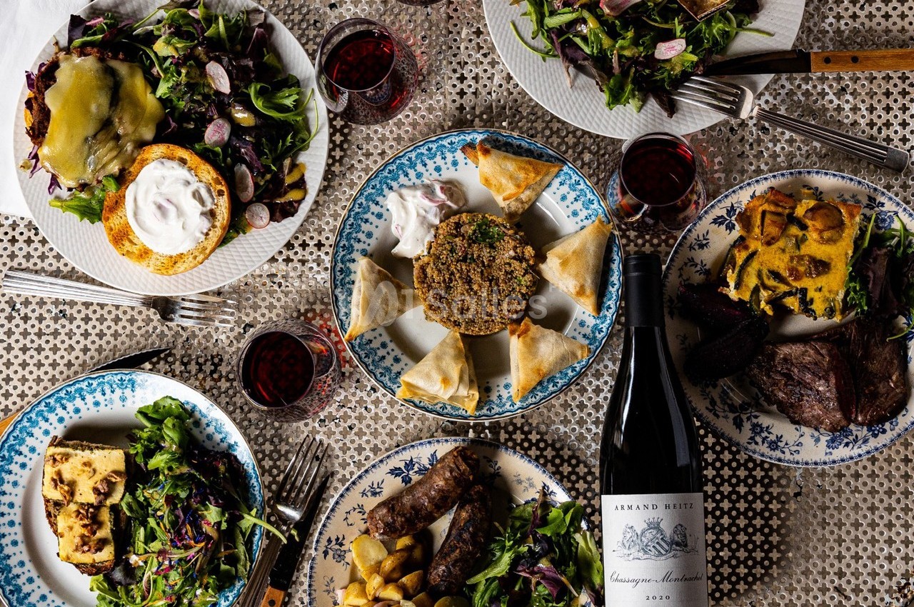 Table dressée avec des assiettes variées de plats, accompagnées de verres de vin rouge et d'une bouteille sur une nappe à…