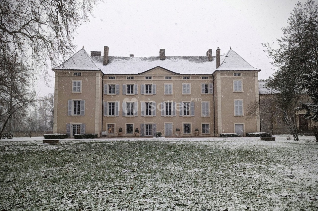 Façade d'un grand bâtiment ancien entouré d'arbres, avec un jardin enneigé au premier plan.