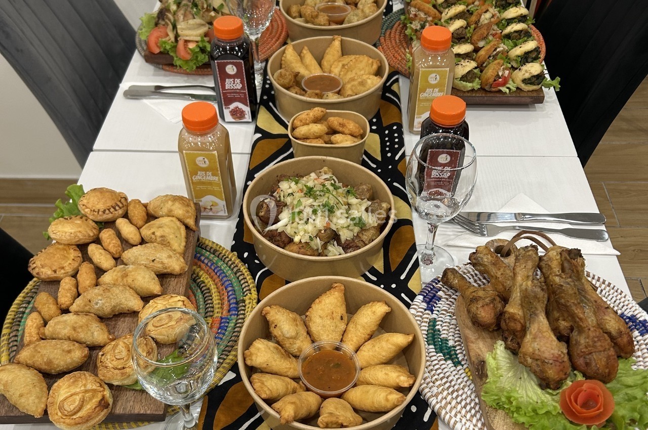 Table garnie de plats variés comprenant empanadas, légumes farcis, pilons de poulet et boissons en bouteille.