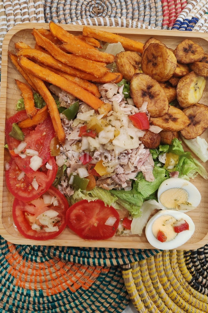 Assiette en bois contenant une salade composée, tomates, œufs durs, patates douces frites et bananes plantains grillées.