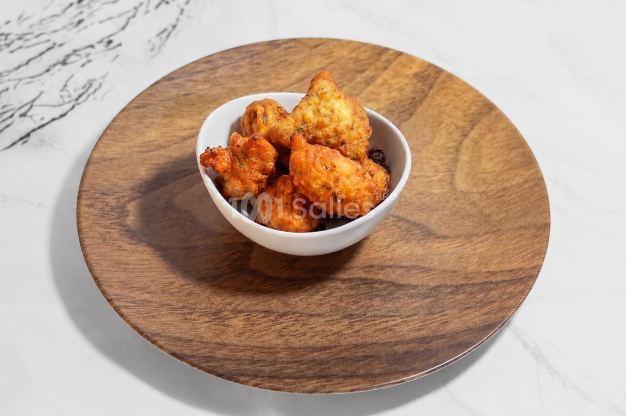 Bol de beignets dorés posés sur une assiette en bois, sur une table en marbre blanc.