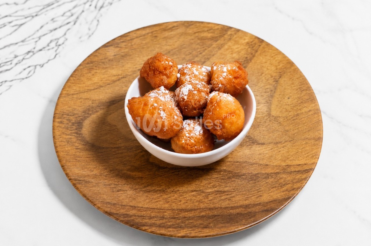 Beignets dorés saupoudrés de sucre glace, servis dans un petit bol blanc sur une assiette en bois.