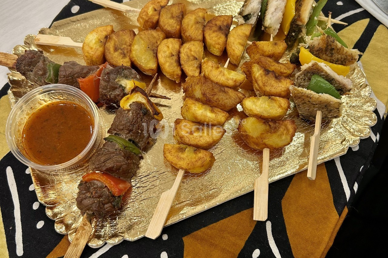 Assortiment de brochettes de viande, légumes, poisson et plantains frits, présenté sur un plateau doré avec une sauce.