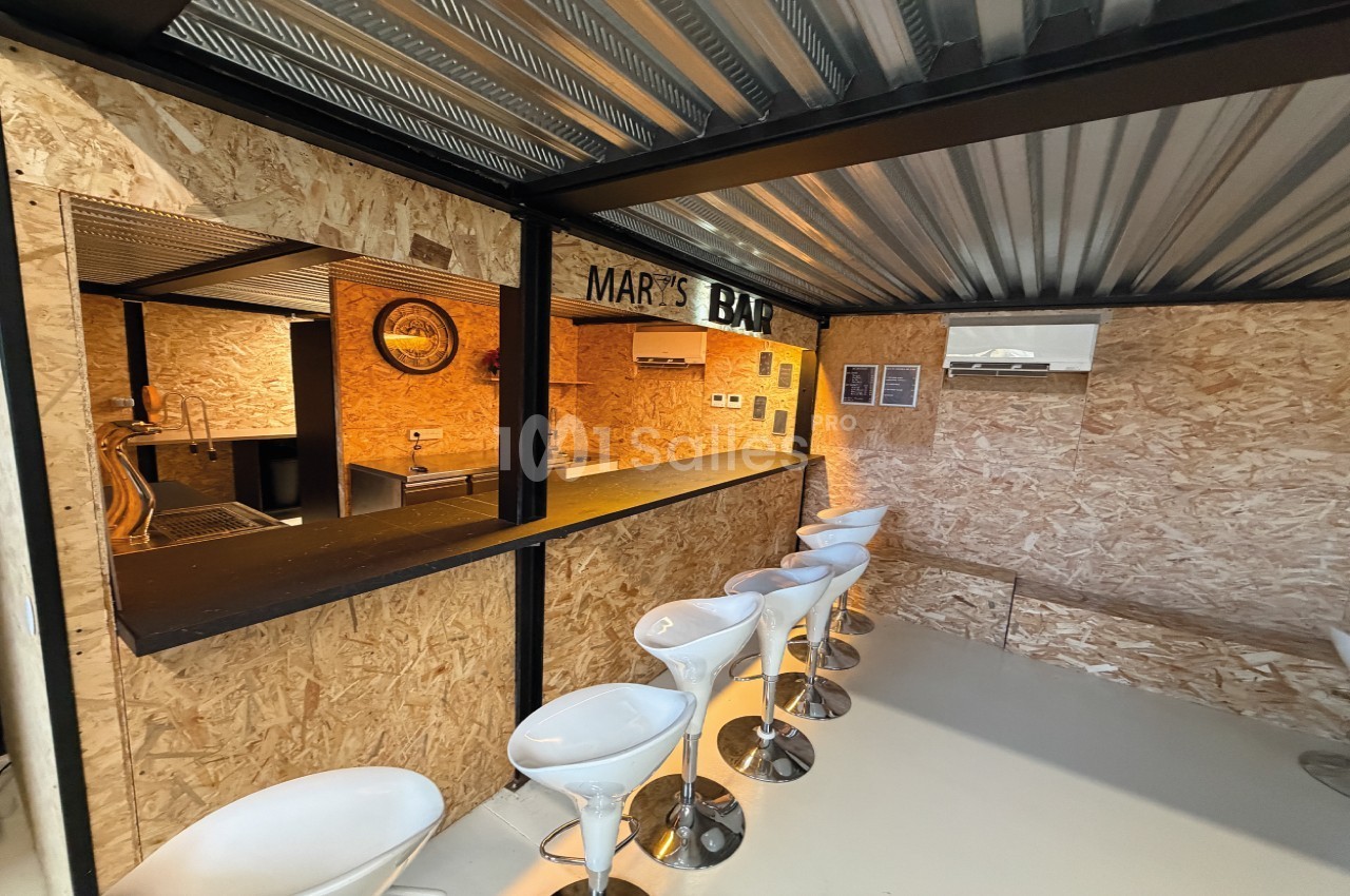 Bar en bois avec comptoir noir, tabourets blancs alignés et décoration intérieure en panneaux OSB.