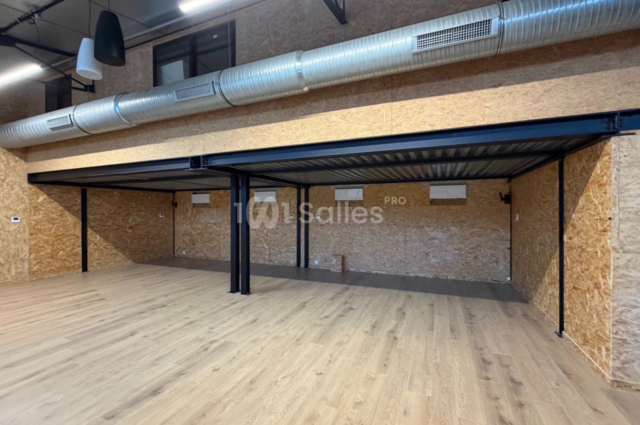 Structure métallique avec mezzanine dans un espace intérieur aux murs en bois et sol en parquet clair.