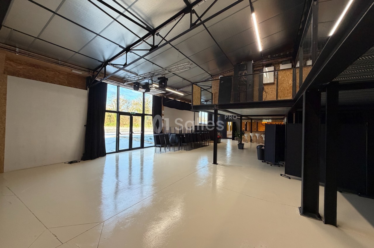 Intérieur d'un espace industriel lumineux avec sol clair, mezzanine métallique et grandes baies vitrées.