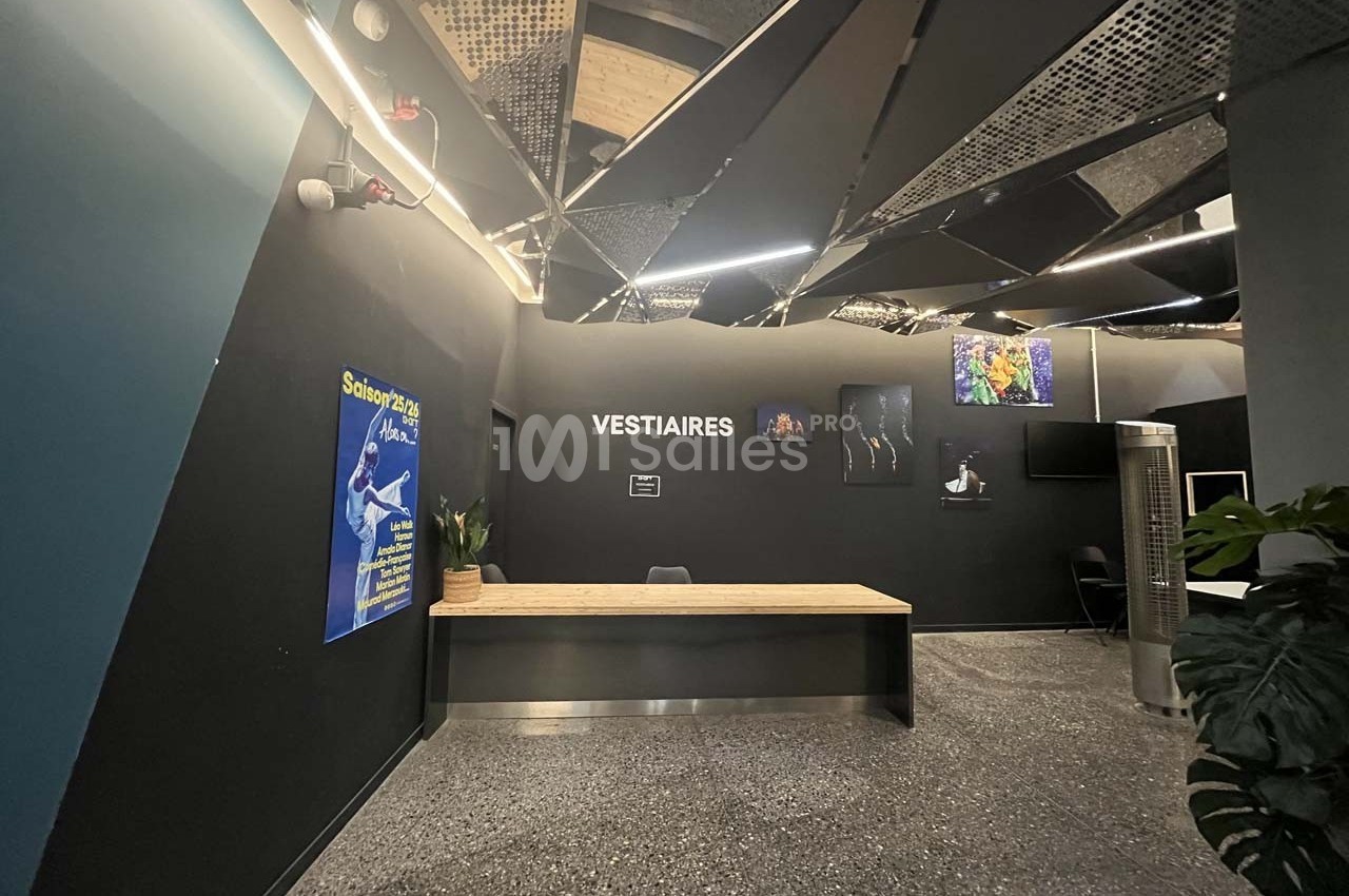 Accueil des vestiaires avec un comptoir en bois, un mur noir, des affiches et un plafond au design moderne.