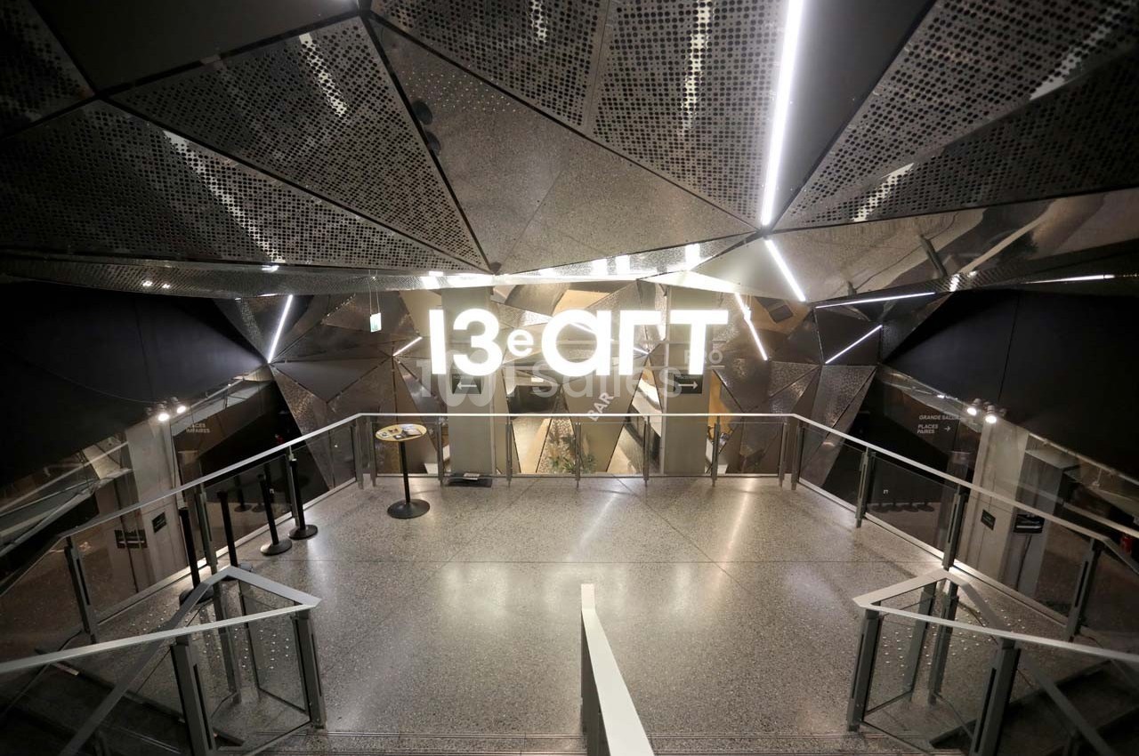 Entrée moderne et éclairée d'un espace nommé ’13e ART’, avec des murs métalliques et un sol en terrazzo.