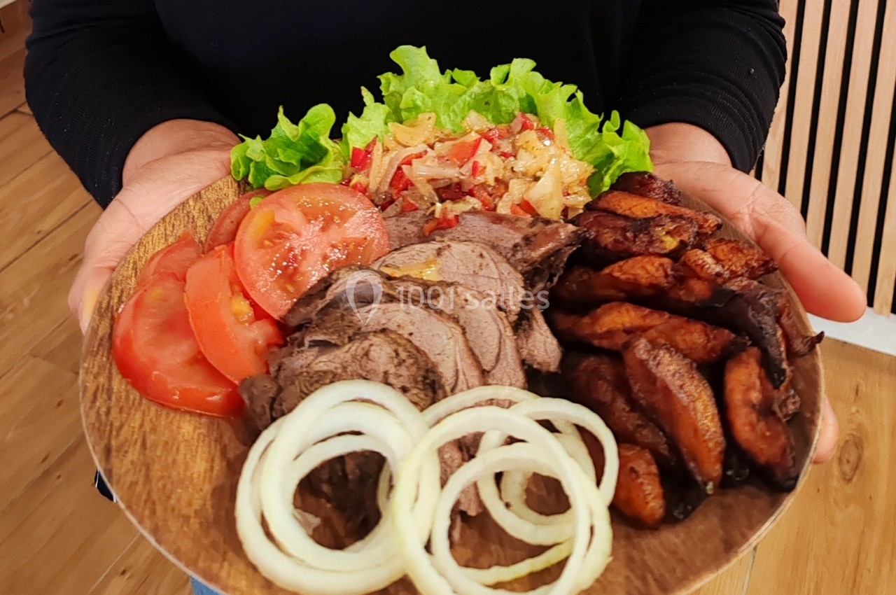 Assiette en bois contenant des tranches de viande, des rondelles d'oignon, des tomates, de la salade et des légumes sautés.