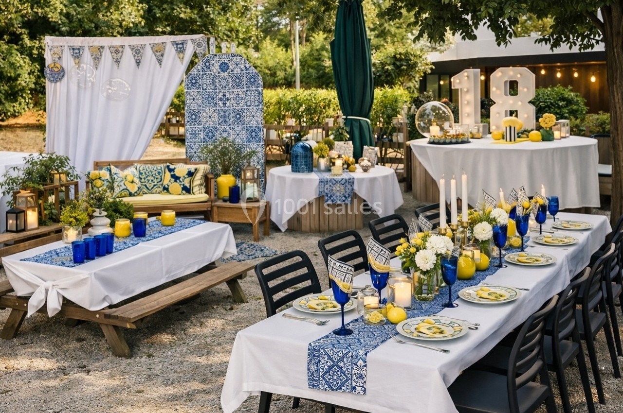 Tables décorées avec des nappes blanches et bleues, bougies, vaisselle colorée et décoration festive en extérieur.