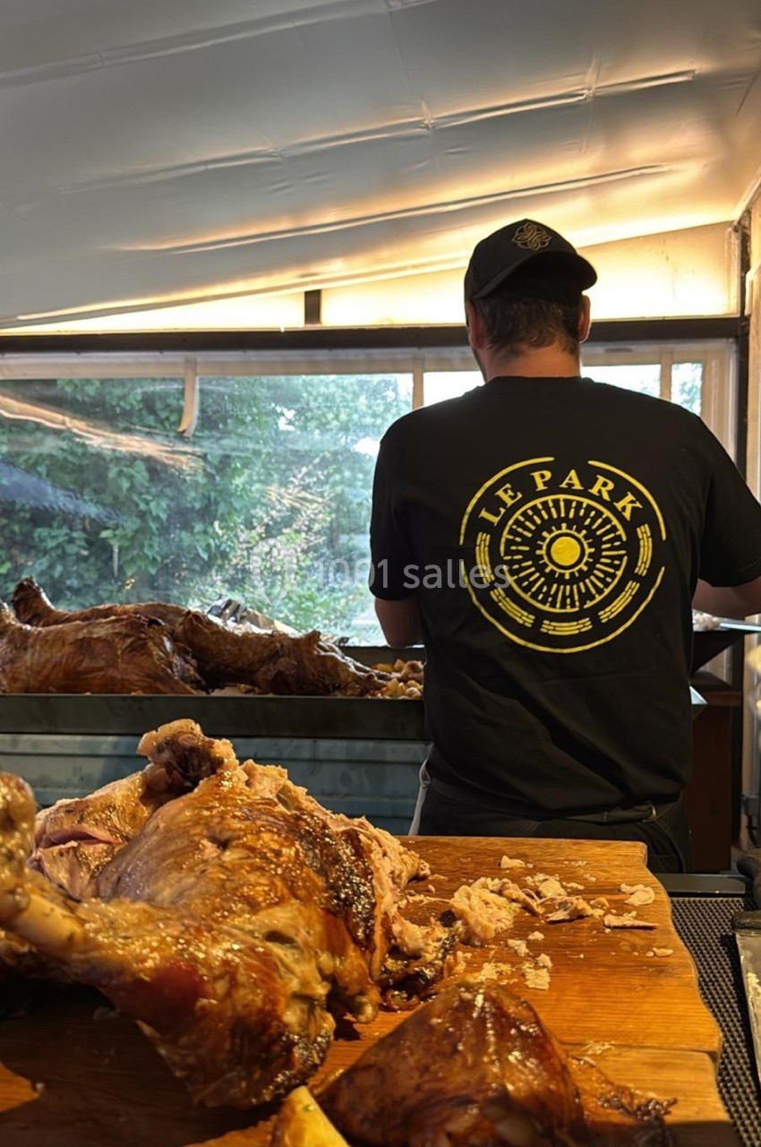 Un cuisinier de dos prépare de la viande rôtie sur un plan de travail en extérieur sous une tente.