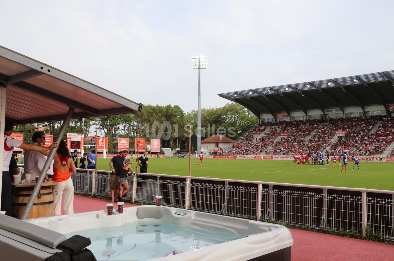 Vue d'un match de rugby dans un stade, avec un jacuzzi au premier plan et des spectateurs en tribunes.