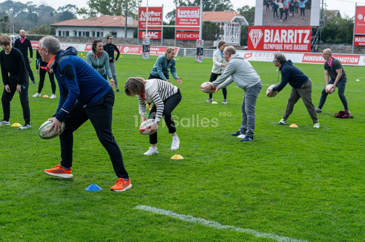 Des personnes participent à un atelier de rugby sur un terrain, tenant des ballons et effectuant des exercices en groupe.