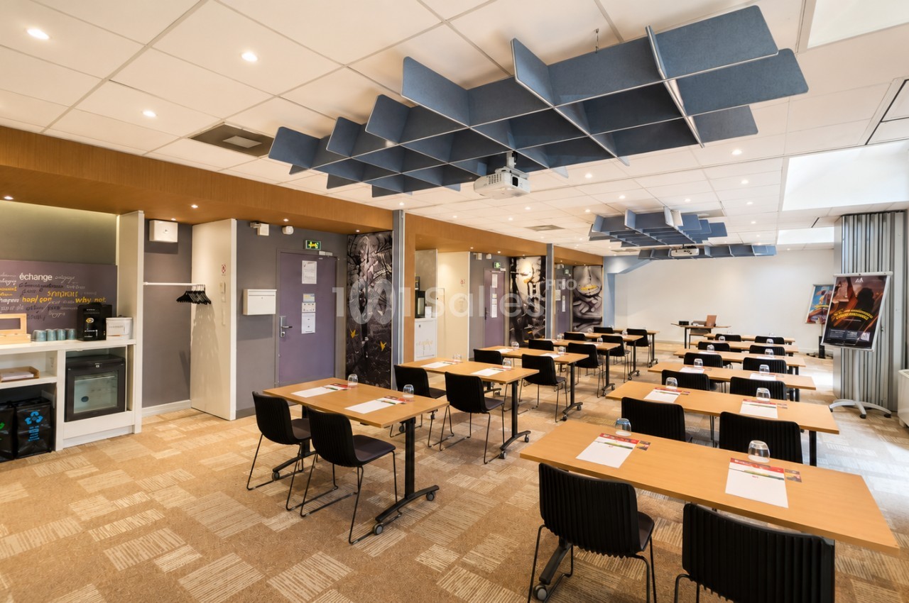 Salle de réunion dressée en U avec tables en bois, chaises noires et panneaux acoustiques bleus au plafond.
