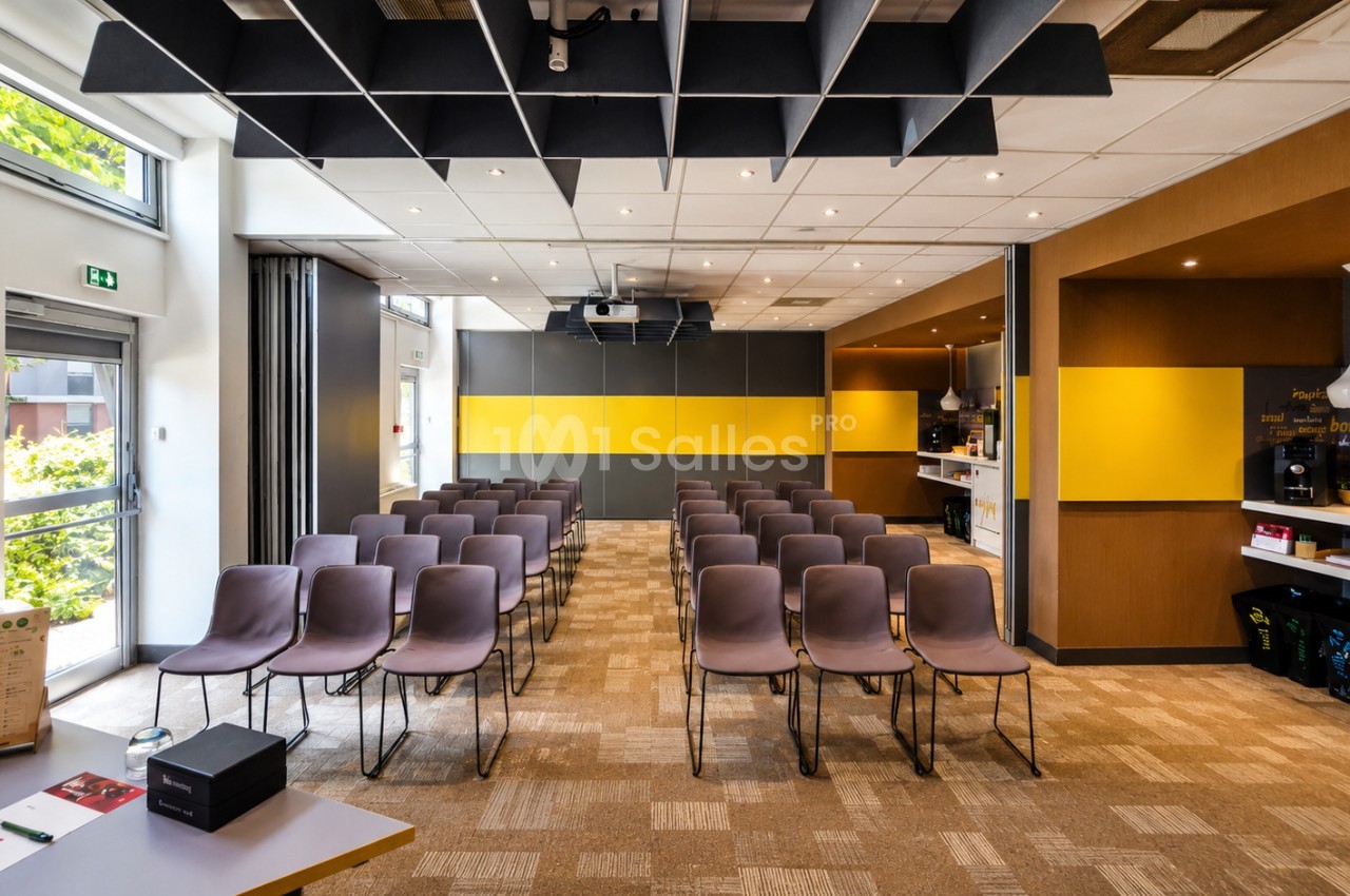 Salle de réunion avec chaises prune alignées en deux blocs, panneaux noirs et jaunes, plafond acoustique, sol parquet.