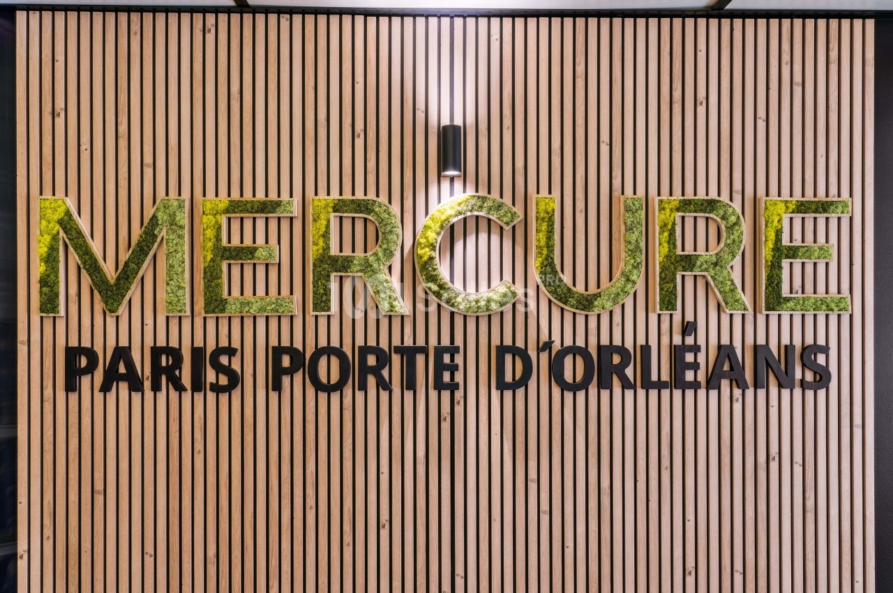 Mur en bois avec le logo ’Mercure Paris Porte d'Orléans’ en lettres dorées et éclairage intégré.