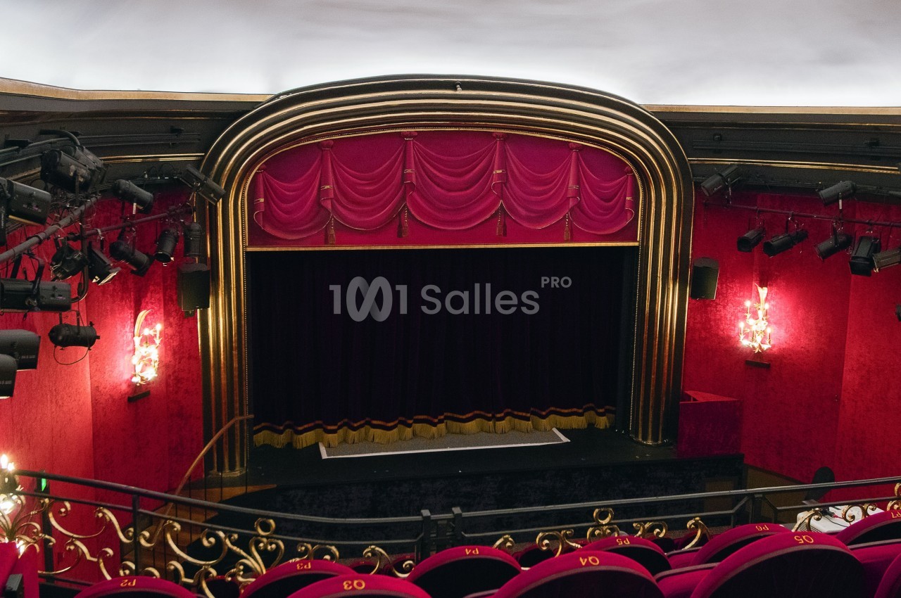 Scène de théâtre avec rideaux rouges, décor doré et sièges en velours rouge dans une salle élégante.