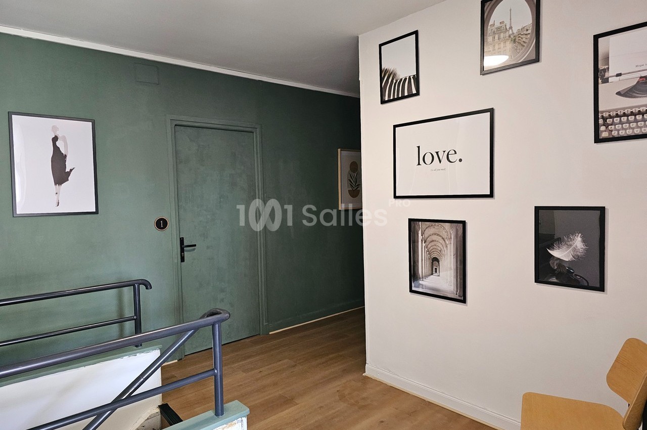 Mur décoré de cadres variés dans un intérieur moderne, avec une porte verte et un sol en bois clair.