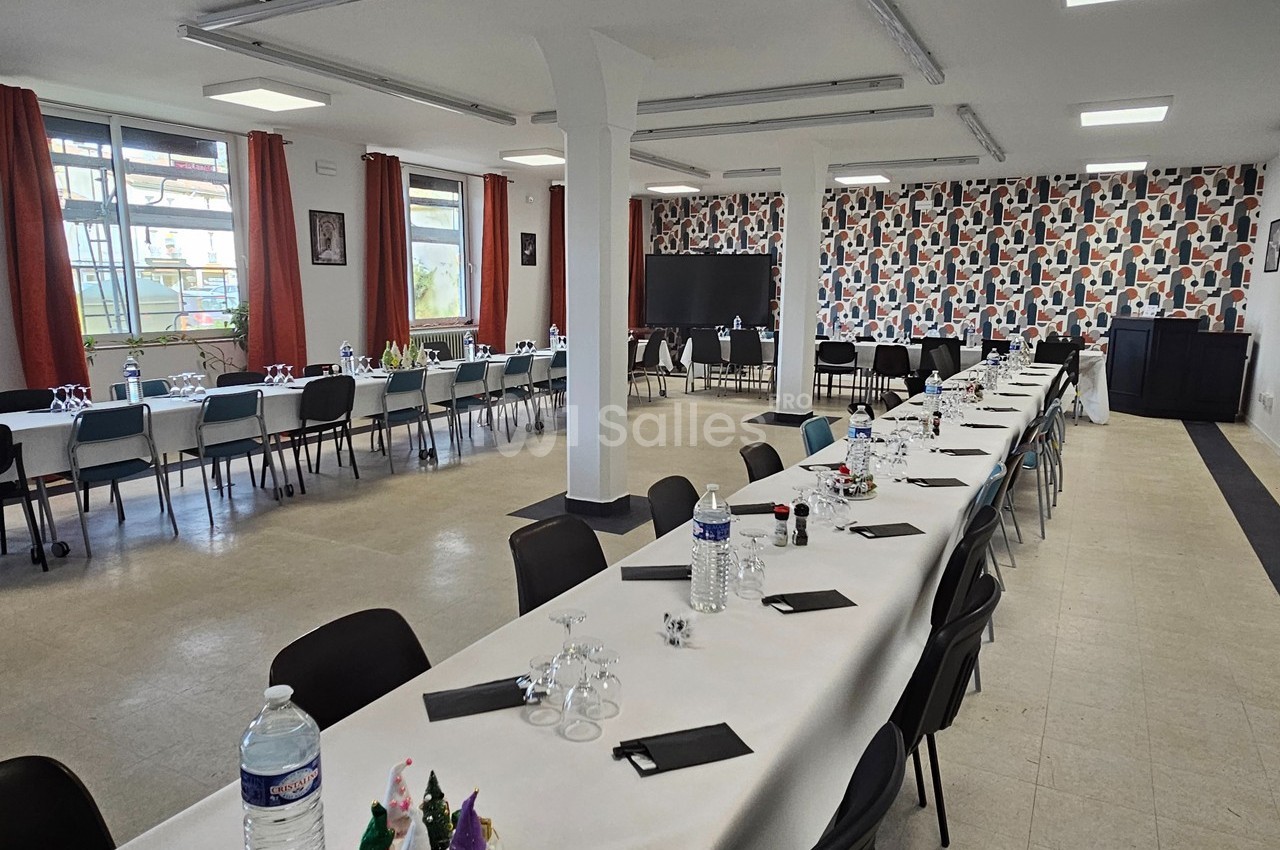 Salle de réception lumineuse avec de longues tables dressées, décorée pour un événement.