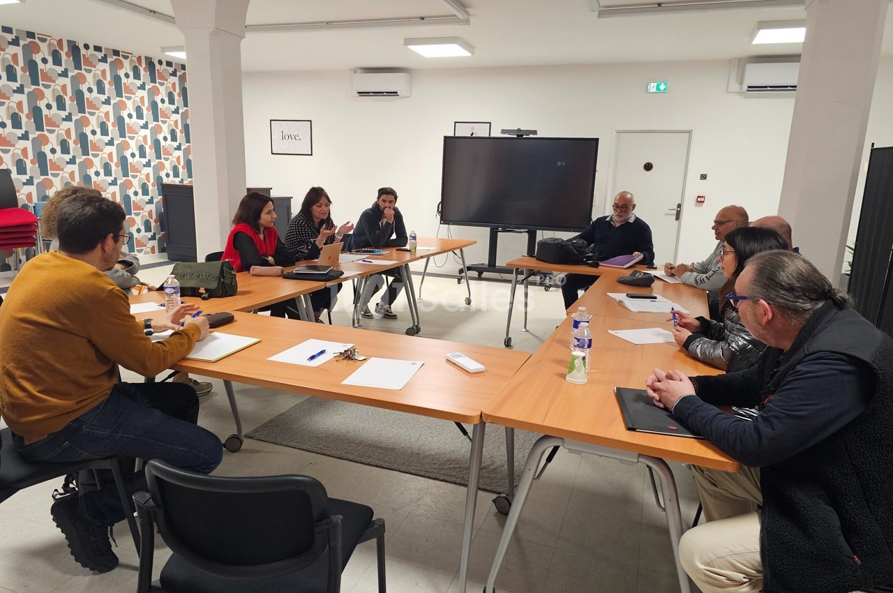 Des personnes assises autour d'une table en réunion dans une salle lumineuse avec un écran et des documents.