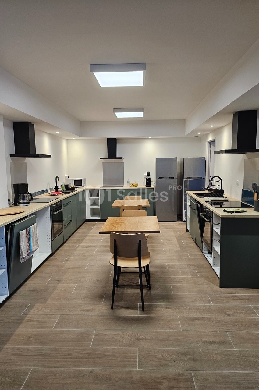 Cuisine moderne avec deux espaces de cuisson, meubles verts, électroménagers en acier inoxydable et tables en bois.