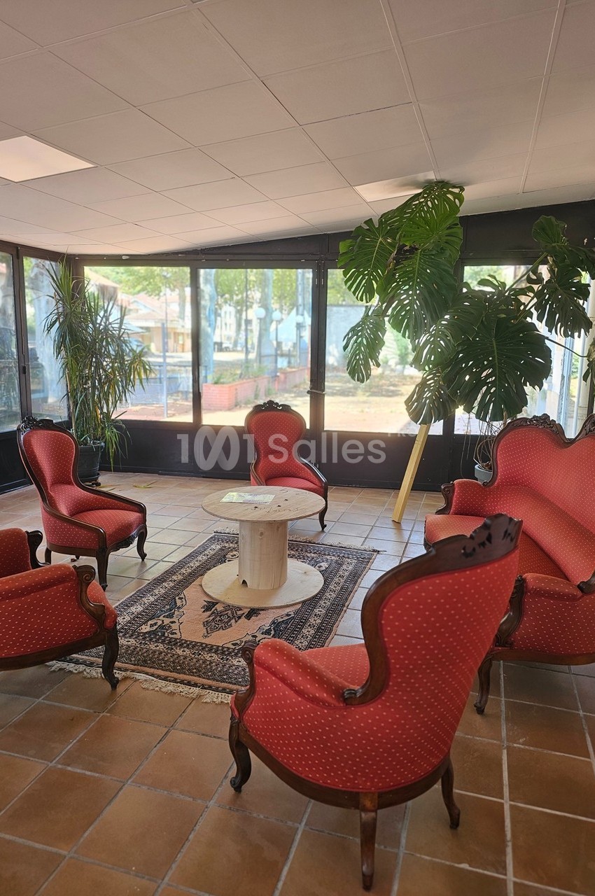 Salon avec fauteuils et canapé rouges, table centrale en marbre, plantes vertes et grandes baies vitrées donnant sur l…