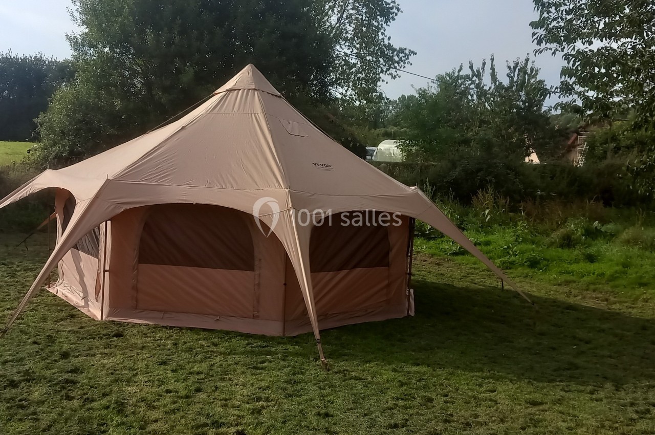 Tente beige spacieuse installée sur une pelouse, entourée d'arbres et de végétation.