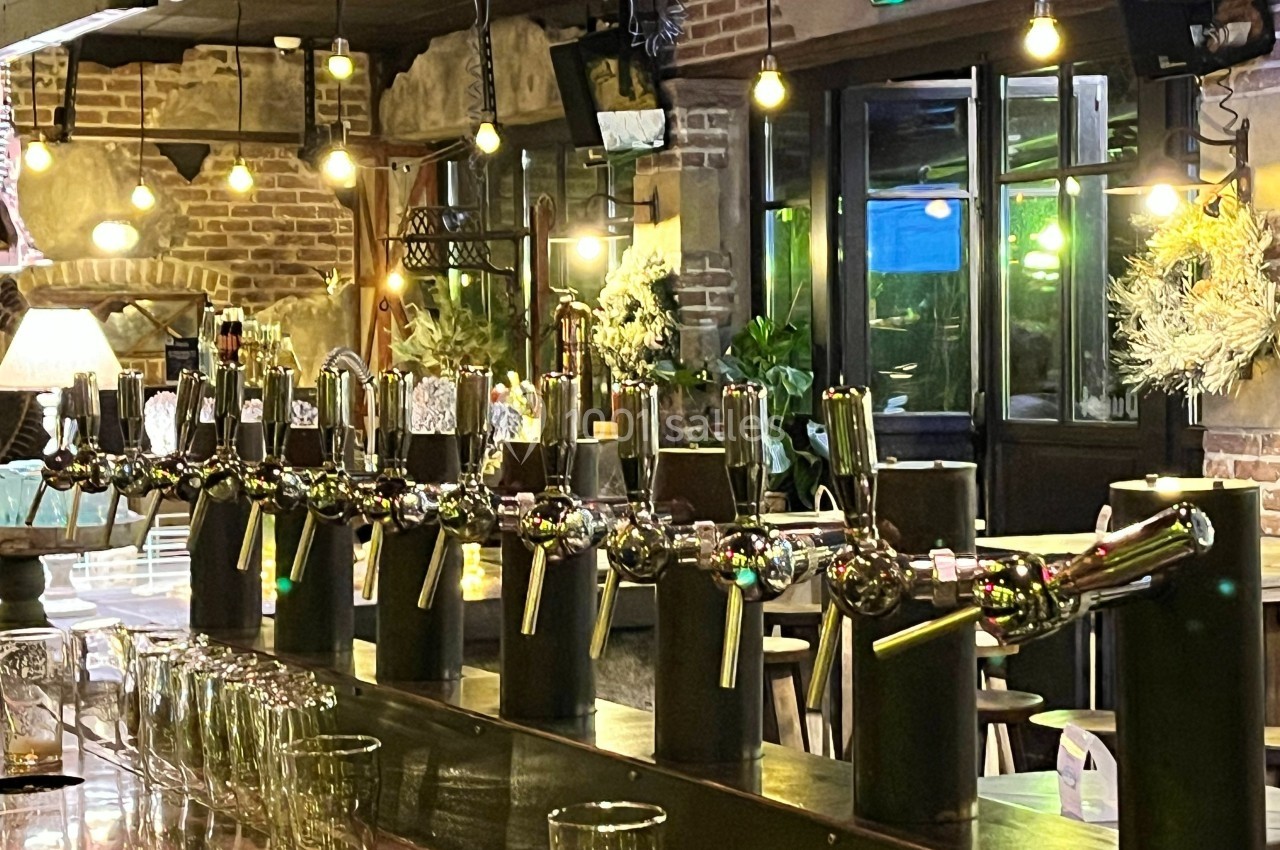 Rangée de tireuses à bière alignées sur un comptoir dans un bar à l'ambiance chaleureuse et éclairage tamisé.