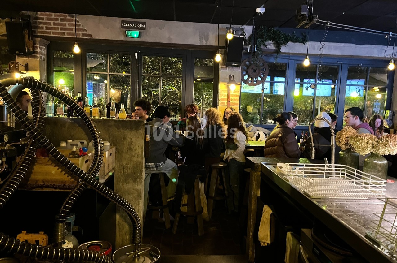 Des personnes assises à un bar dans une ambiance chaleureuse avec des lumières tamisées et une grande baie vitrée.