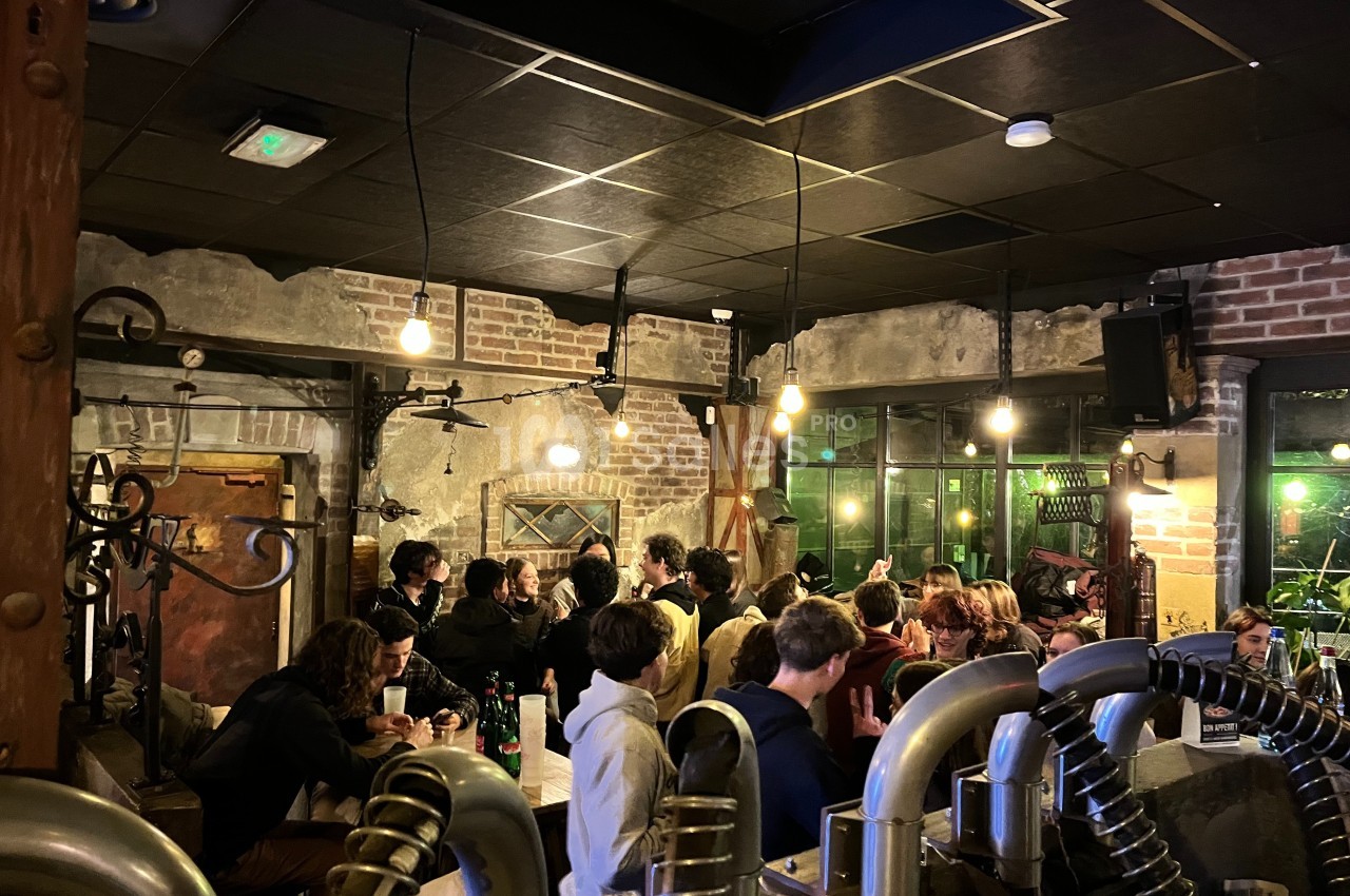 Groupe de personnes discutant et partageant un moment convivial dans un bar à l'ambiance industrielle et chaleureuse.